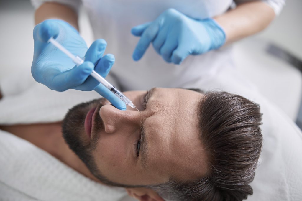 Middle aged man grimaces of pain while skilled cosmetologist does injection